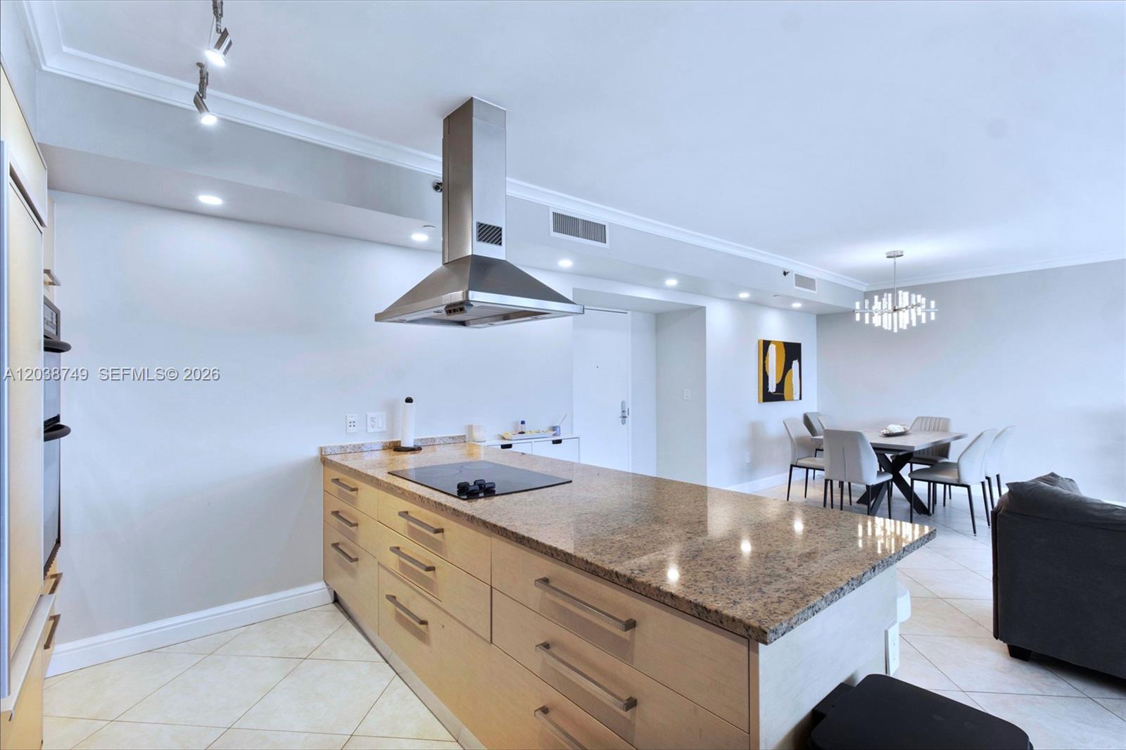 A kitchen island with a cooktop and granite countertop sits in an open-concept living space — HALLANDALE BEACH, FL