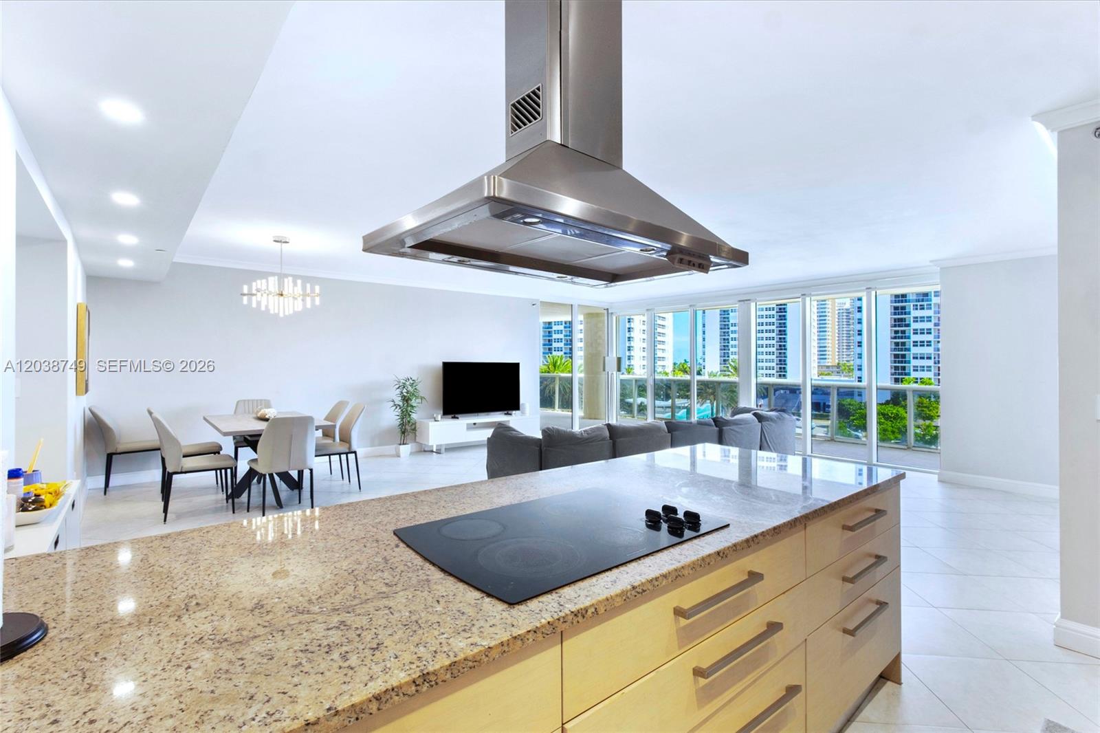 A kitchen island with a cooktop overlooks an open-concept living and dining area — HALLANDALE BEACH, FL