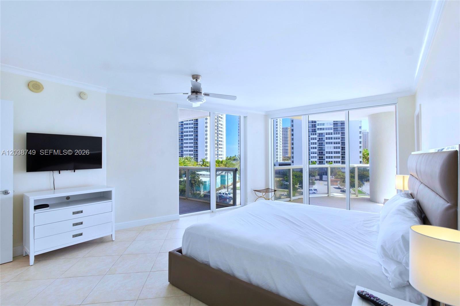 A bedroom features a bed, a white dresser with a television, and floor-to-ceiling balcony doors — HALLANDALE BEACH, FL