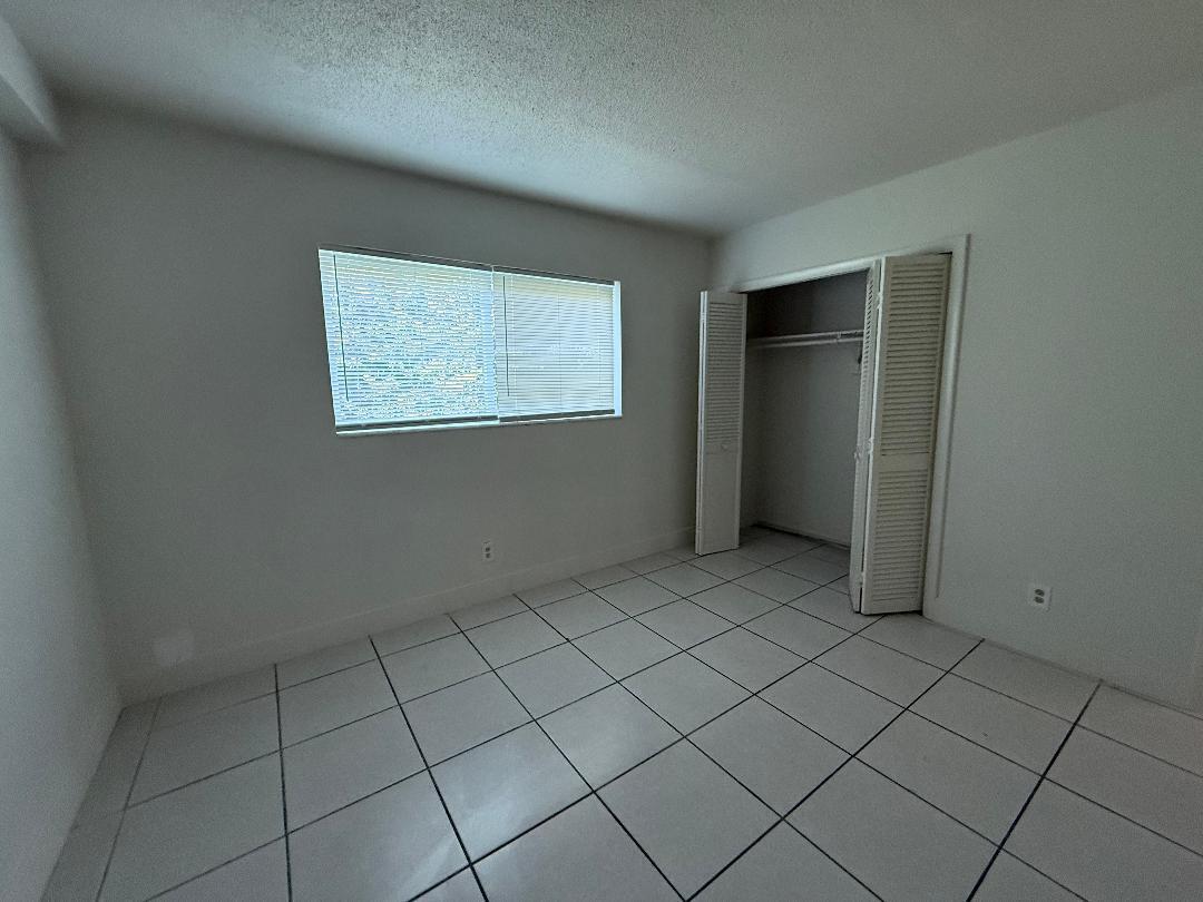 An empty bedroom features white walls, white tile flooring, a window with blinds, and a closet — 1913 NE 2nd Street # 4, Pompano Beach FL 33060, POMPANO BEACH, FL