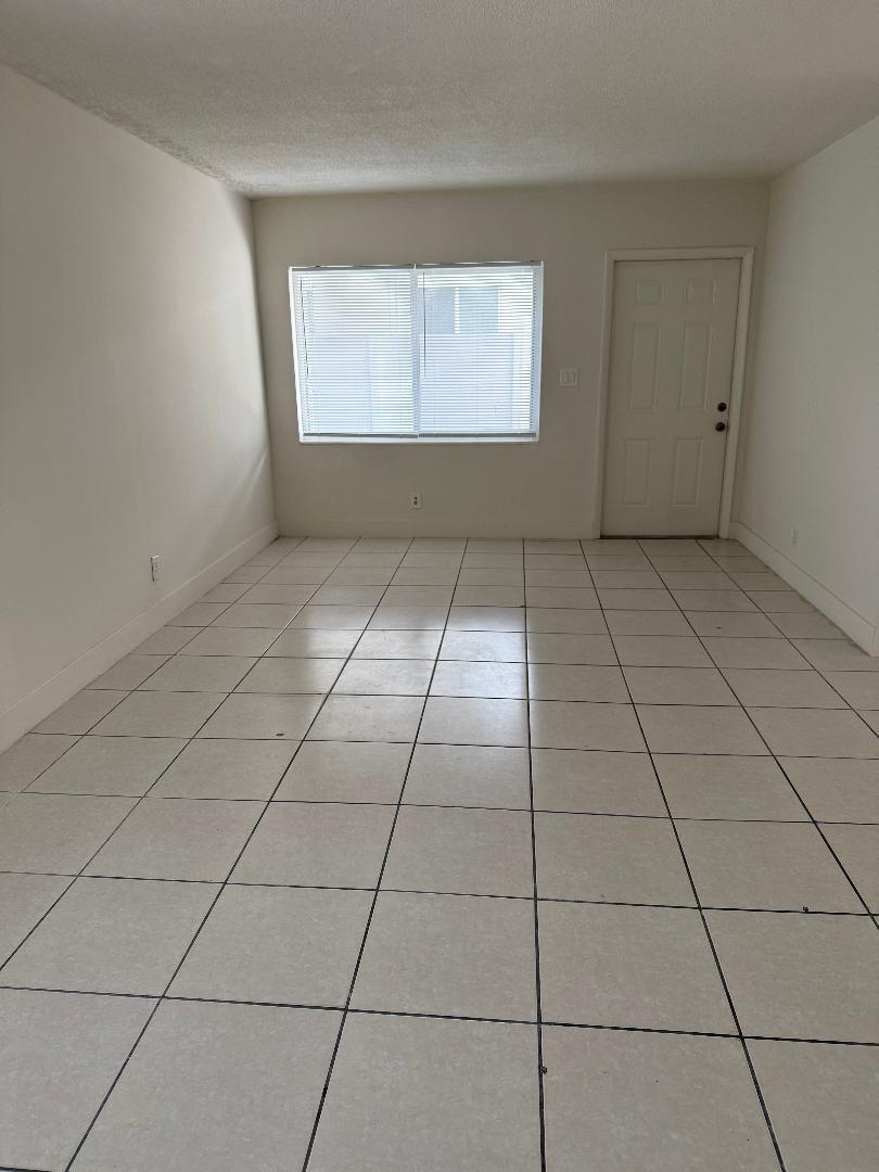 An empty room with white walls, light-colored tile flooring, a window with blinds, and a door — 1913 NE 2nd Street # 4, Pompano Beach FL 33060, POMPANO BEACH, FL