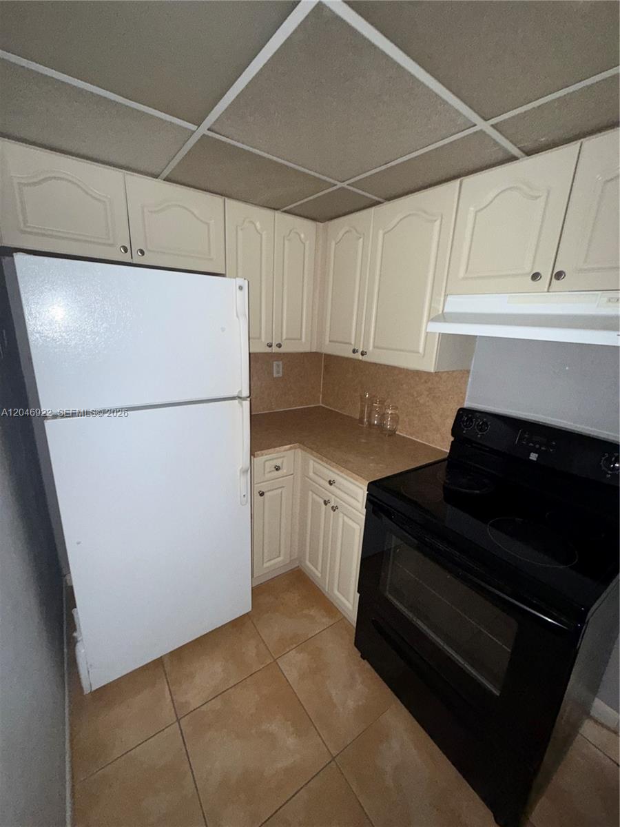 A small kitchen features white cabinets, a white refrigerator, a black stove, and tiled flooring — 6960 Miami Gardens Dr # 431A, Hialeah FL 33015, HIALEAH, FL