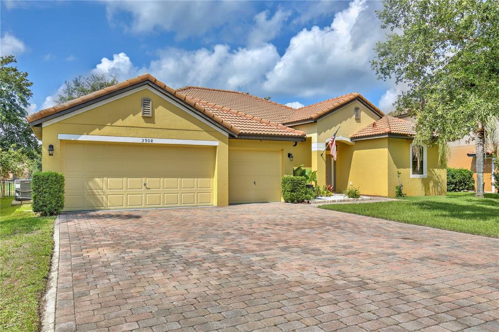 A yellow single-story house with a tiled roof, three-car garage, and a brick paver driveway — 3908 COASTAL BREEZE DRIVE, KISSIMMEE, FL