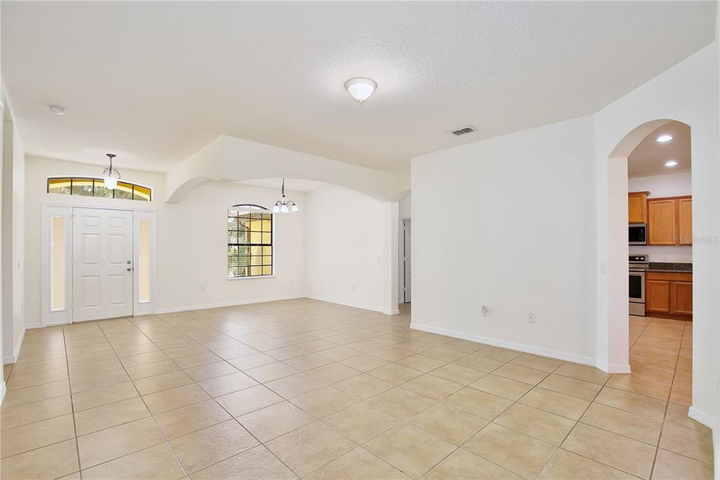 An open-concept living area features beige tile flooring, white walls, and an arched kitchen entryway — 3908 COASTAL BREEZE DRIVE, KISSIMMEE, FL