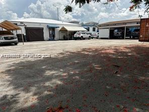 An exterior view of a commercial building with a gravel lot and covered parking areas — 918 E 2nd Ave, Hialeah FL 33010, HIALEAH, FL