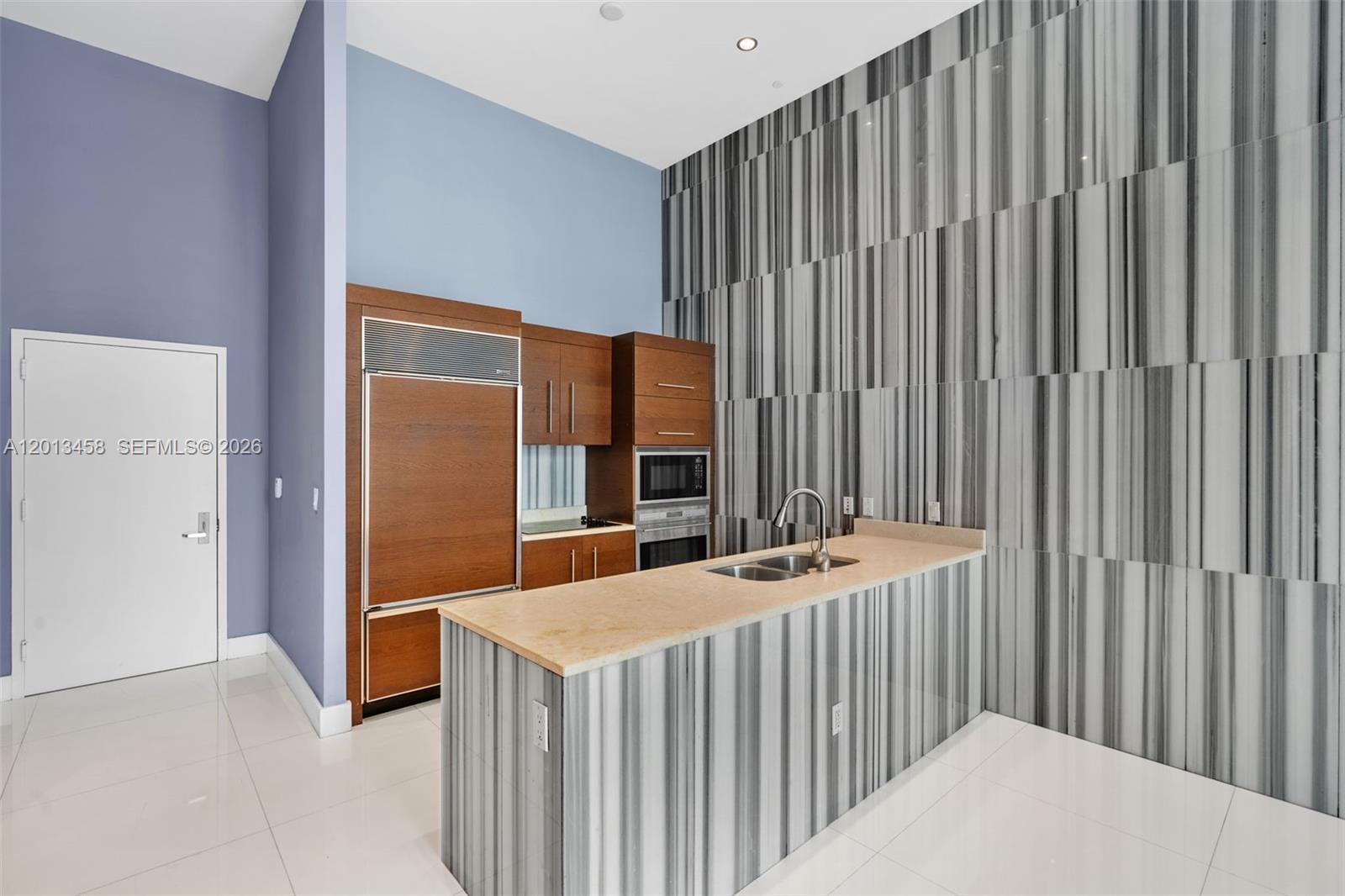 A kitchen features wood cabinetry, a stone-topped island, and a tall, striped marble accent wall — 475 Brickell Ave # 2812, Miami FL 33131, MIAMI, FL