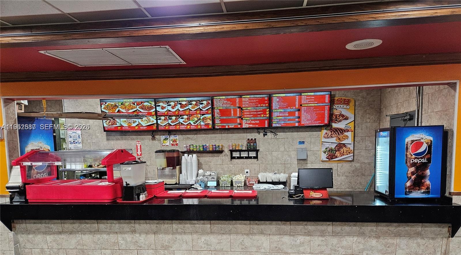 A commercial kitchen counter features menu boards, a beverage cooler, and food preparation equipment — 820 W Sample Rd, Pompano Beach FL 33064, POMPANO BEACH, FL
