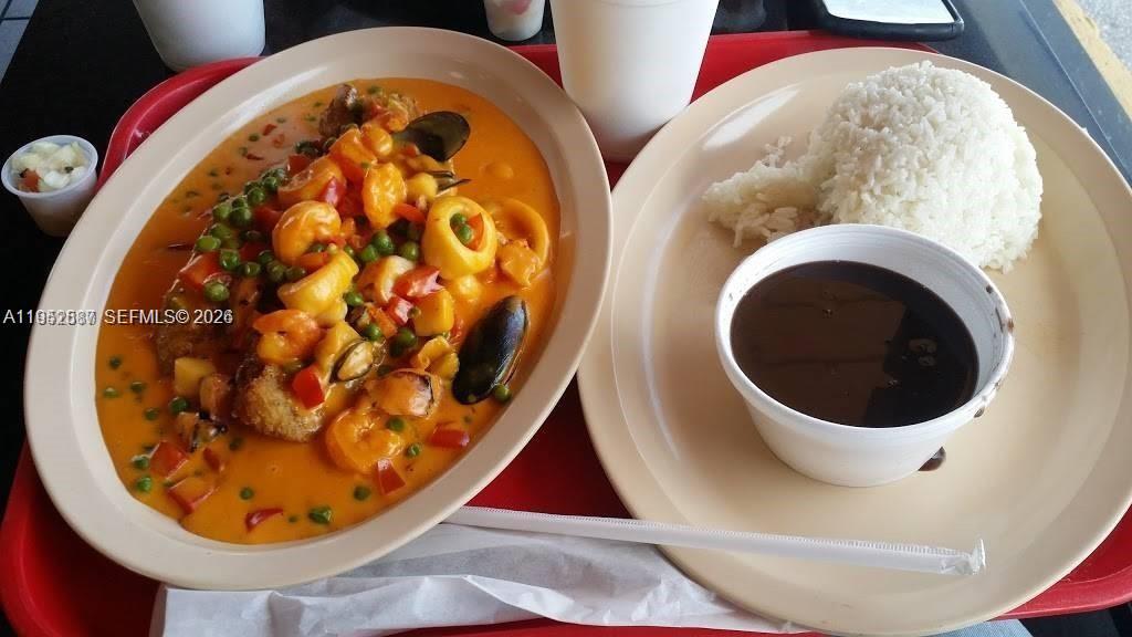 A plate of seafood in a creamy sauce sits next to rice and black beans — 820 W Sample Rd, Pompano Beach FL 33064, POMPANO BEACH, FL