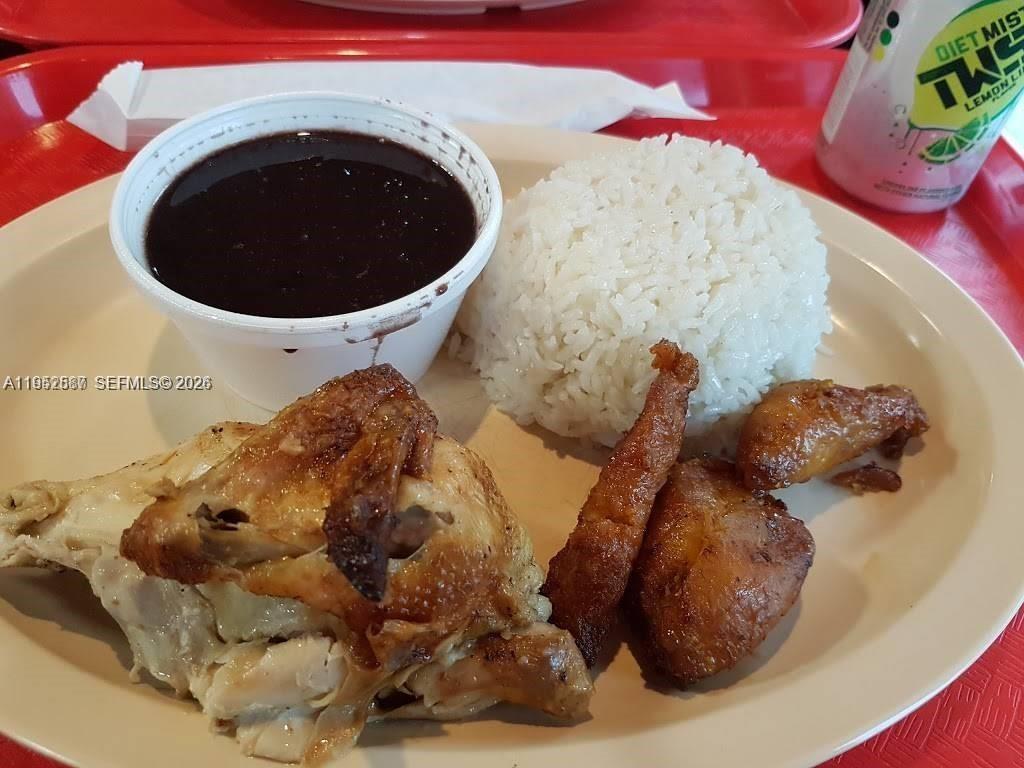 A plate of roasted chicken, white rice, and black beans sits on a red tray — 820 W Sample Rd, Pompano Beach FL 33064, POMPANO BEACH, FL