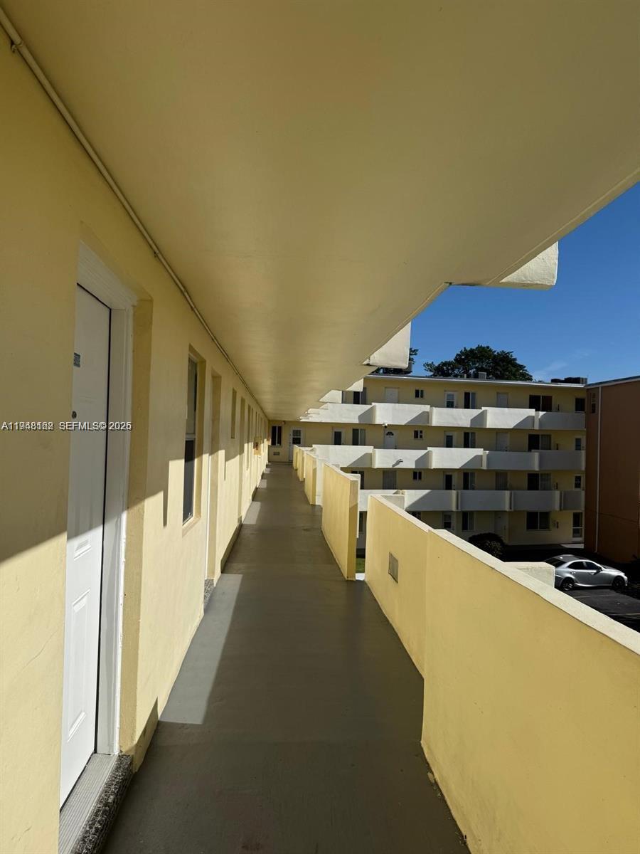 An exterior open-air walkway leads along a yellow apartment building with a parking lot below — 1201 NE 191st St # G313, Miami FL 33179, MIAMI, FL