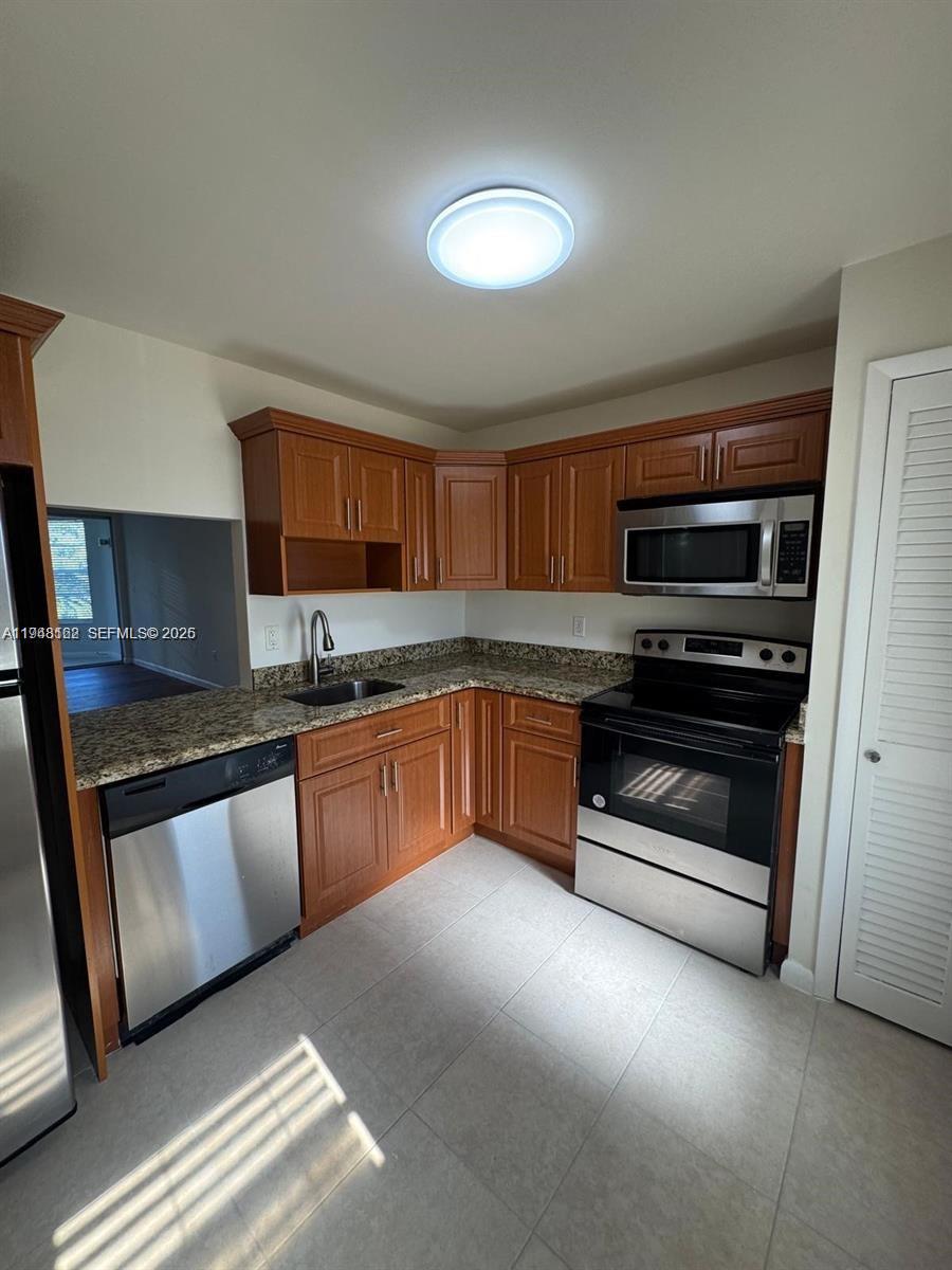 A kitchen features wood cabinets, granite countertops, stainless steel appliances, and light-colored tile flooring — 1201 NE 191st St # G313, Miami FL 33179, MIAMI, FL