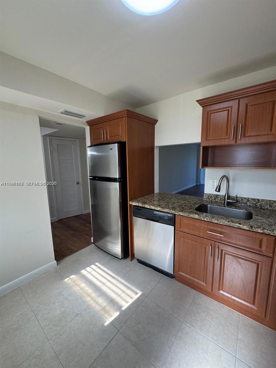 A kitchen features wood cabinets, granite countertops, stainless steel appliances, and tile flooring — 1201 NE 191st St # G313, Miami FL 33179, MIAMI, FL