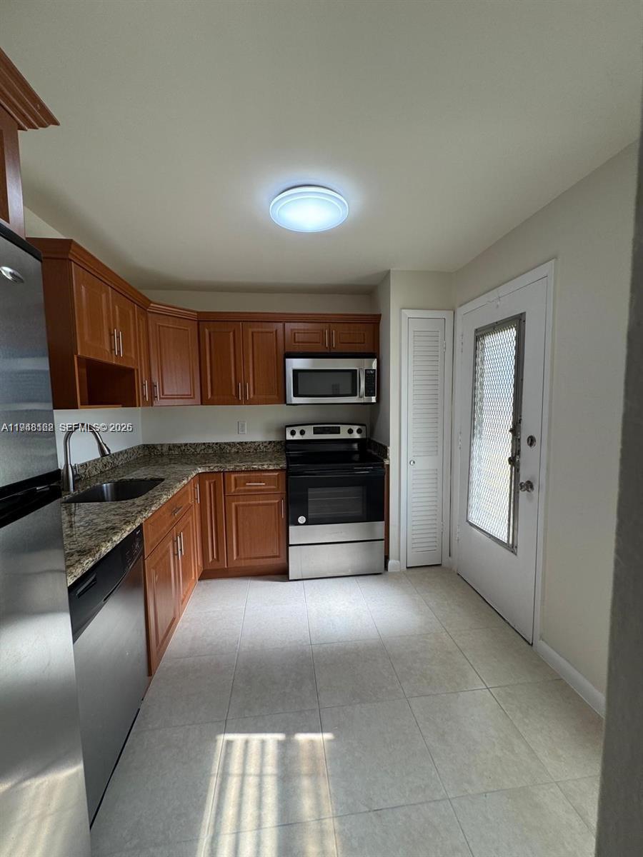 A kitchen features wood cabinets, granite countertops, stainless steel appliances, and light tile flooring — 1201 NE 191st St # G313, Miami FL 33179, MIAMI, FL