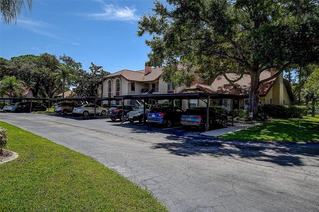 A multi-story apartment building with covered parking spaces and mature trees in the foreground — 2632 ENTERPRISE ROAD E UNIT A12, CLEARWATER, FL
