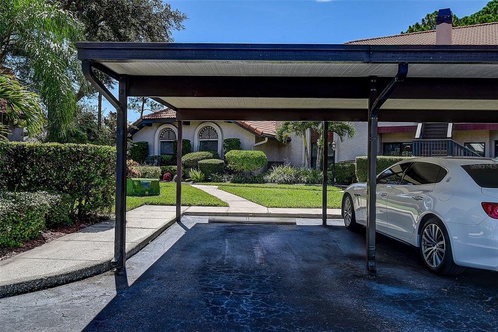 A white sedan is parked under a metal carport in front of a residential building — 2632 ENTERPRISE ROAD E UNIT A12, CLEARWATER, FL