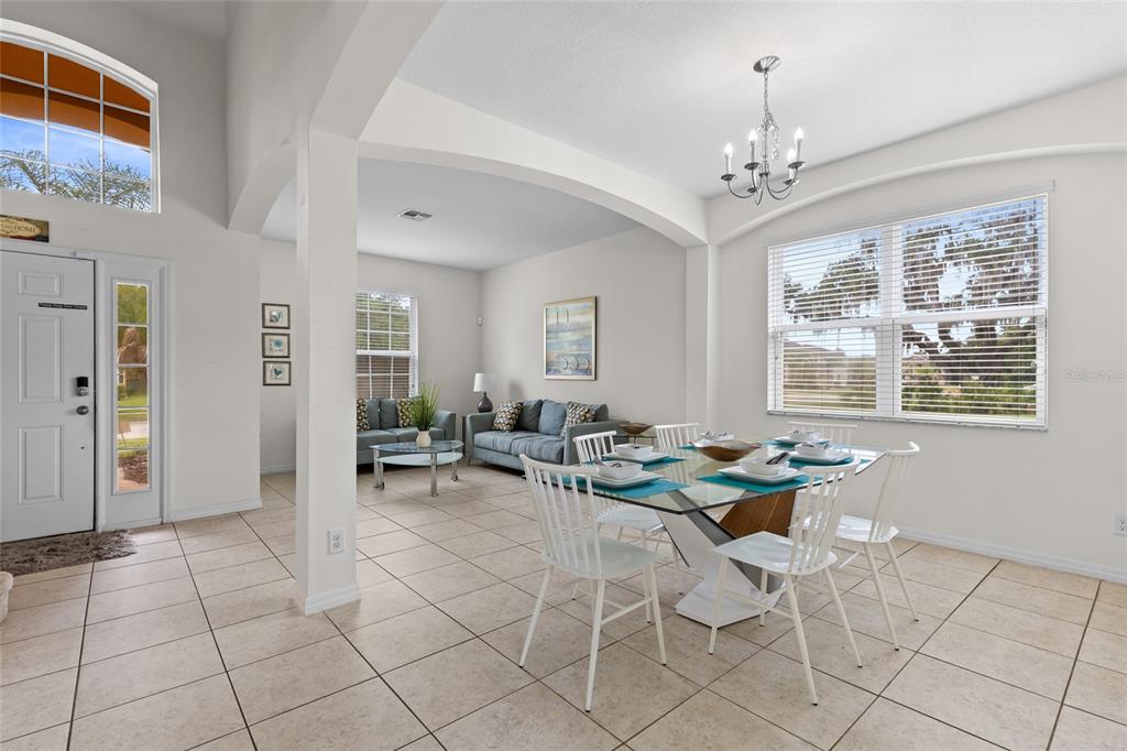A bright dining area with a glass table and chandelier opens into a living room — 2501 DHARMA CIRCLE, KISSIMMEE, FL