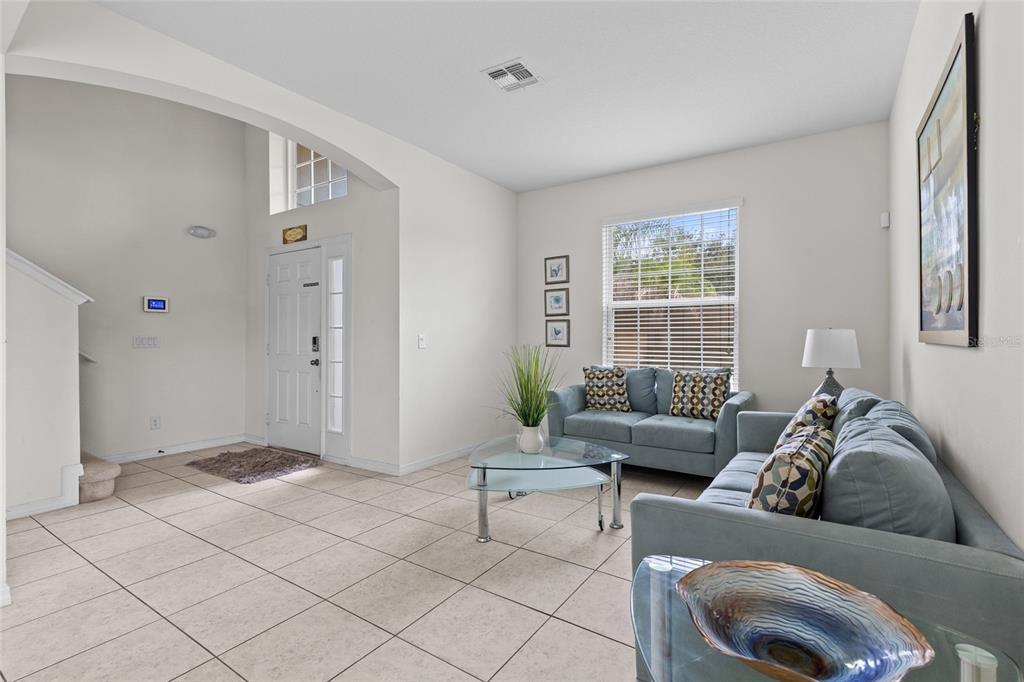 A living room with light tile floors, blue sofas, a glass coffee table, and entryway — 2501 DHARMA CIRCLE, KISSIMMEE, FL