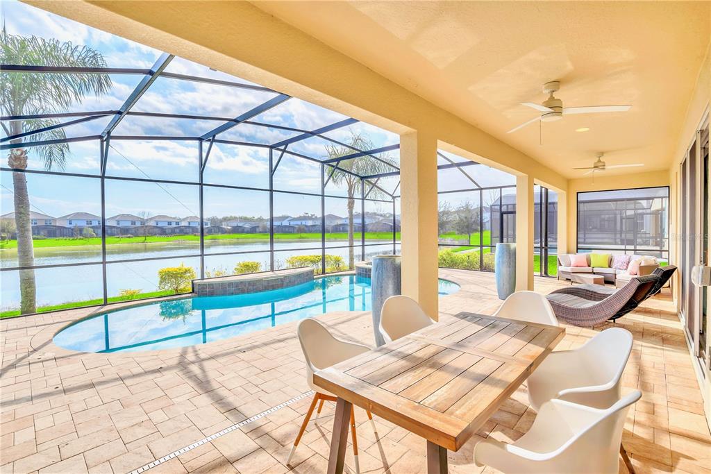 A covered patio features a dining table, lounge seating, and a pool overlooking a lake — 537 MARCELLO BOULEVARD, KISSIMMEE, FL