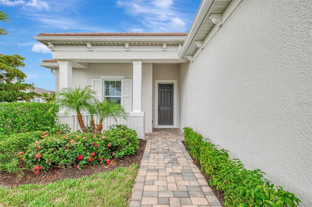 A paved walkway leads to the front entrance of a house with a dark door — 12365 VIESTE COURT, VENICE, FL