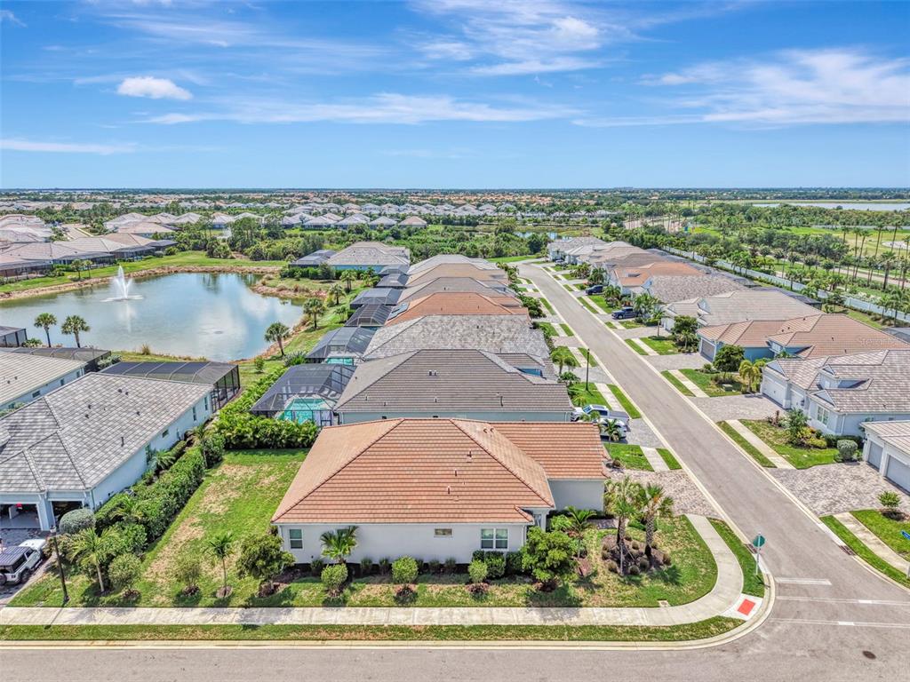 An aerial view of a suburban neighborhood featuring houses with tiled roofs and a pond — 12365 VIESTE COURT, VENICE, FL