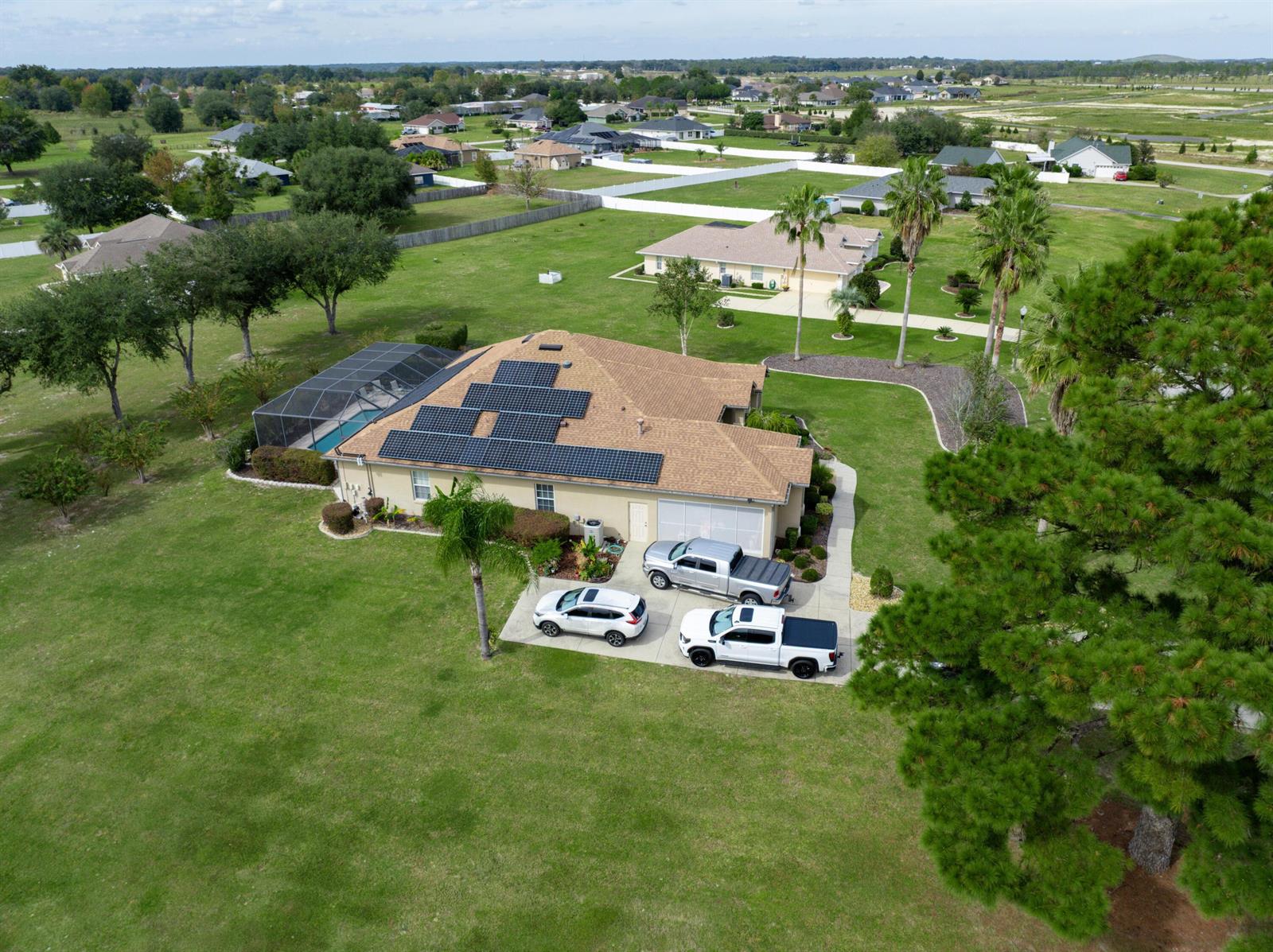 An aerial view shows a house with solar panels, a pool cage, and three parked vehicles — 9908 SE 67th Avenue Road, FL 34420, FL