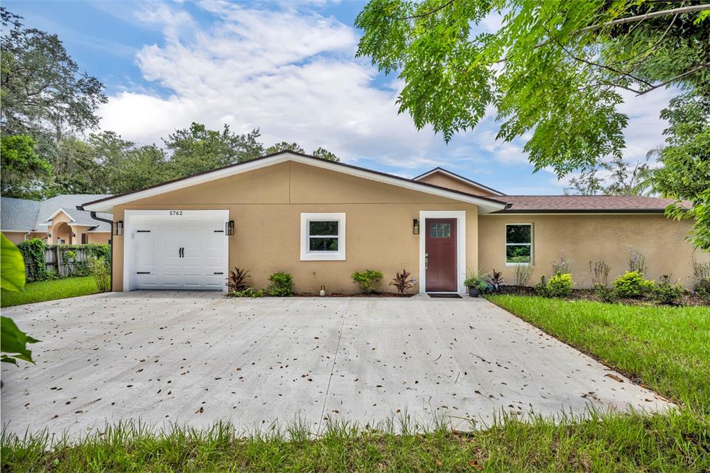 A single-story house with a tan stucco exterior, a white garage door, and a concrete driveway — 5762 SHERYL ANITA STREET, OVIEDO, FL