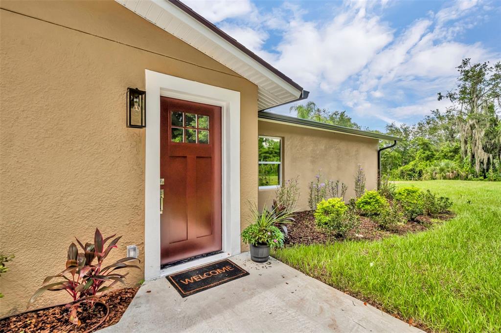 A brown front door with a window sits on a concrete porch beside a house — 5762 SHERYL ANITA STREET, OVIEDO, FL