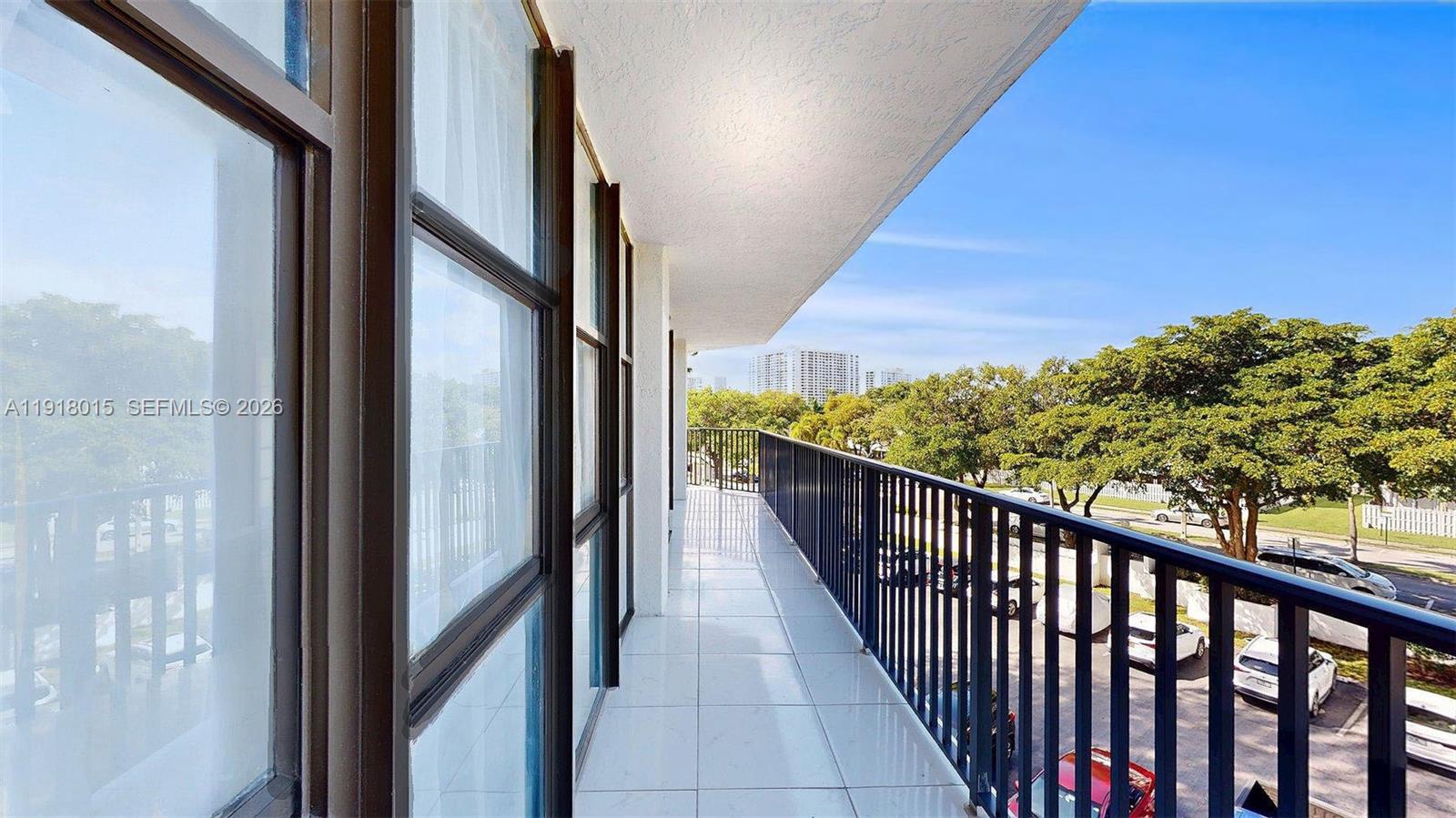 A long balcony with white tile flooring and a black metal railing overlooks a parking lot — 1000 Parkview Dr # 431, Hallandale Beach FL 33009, HALLANDALE BEACH, FL