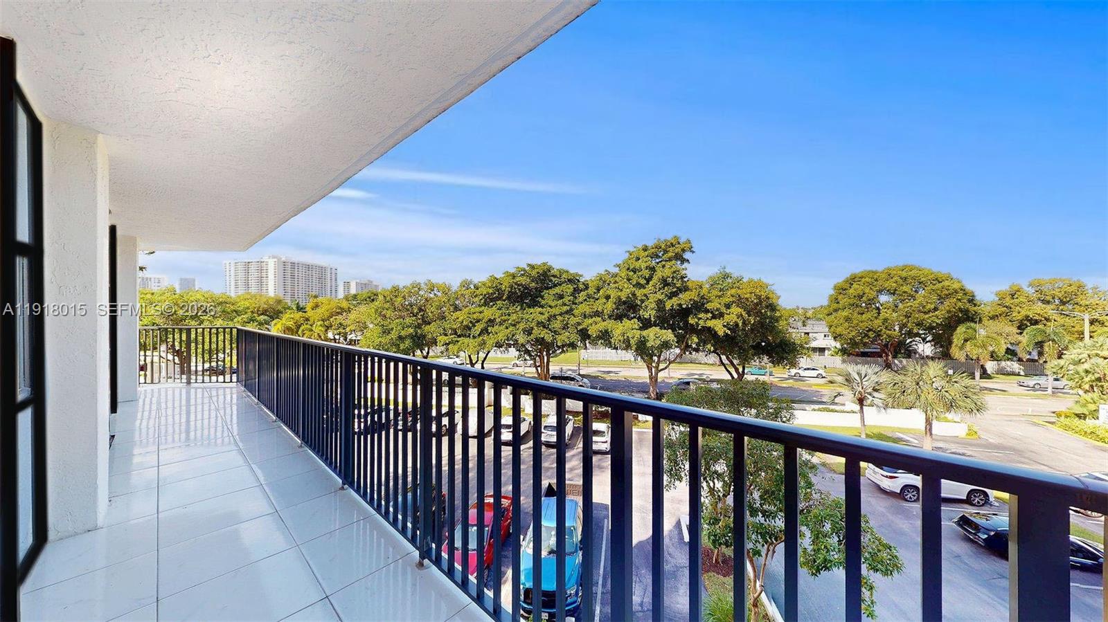 A tiled balcony with a black metal railing overlooks a parking lot and trees — 1000 Parkview Dr # 431, Hallandale Beach FL 33009, HALLANDALE BEACH, FL