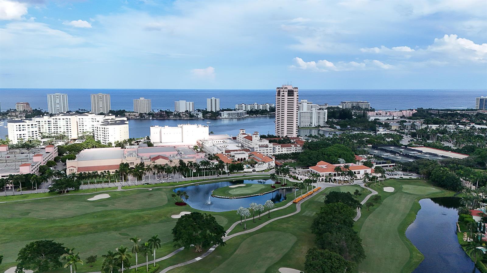 An aerial view shows a golf course with ponds, surrounding buildings, and the ocean beyond — 105 E Camino Real # 912, Boca Raton FL 33432, BOCA RATON, FL