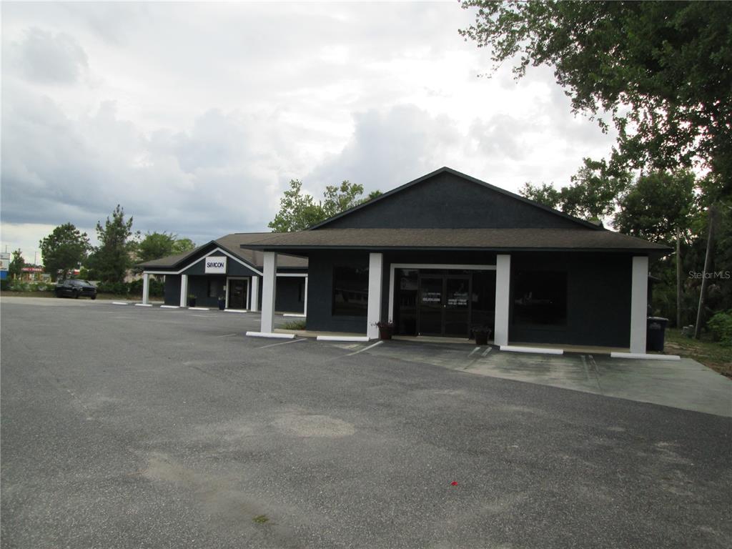 A dark-painted commercial building with white columns and a large asphalt parking lot — 100 W BURLEIGH BOULEVARD, TAVARES, FL