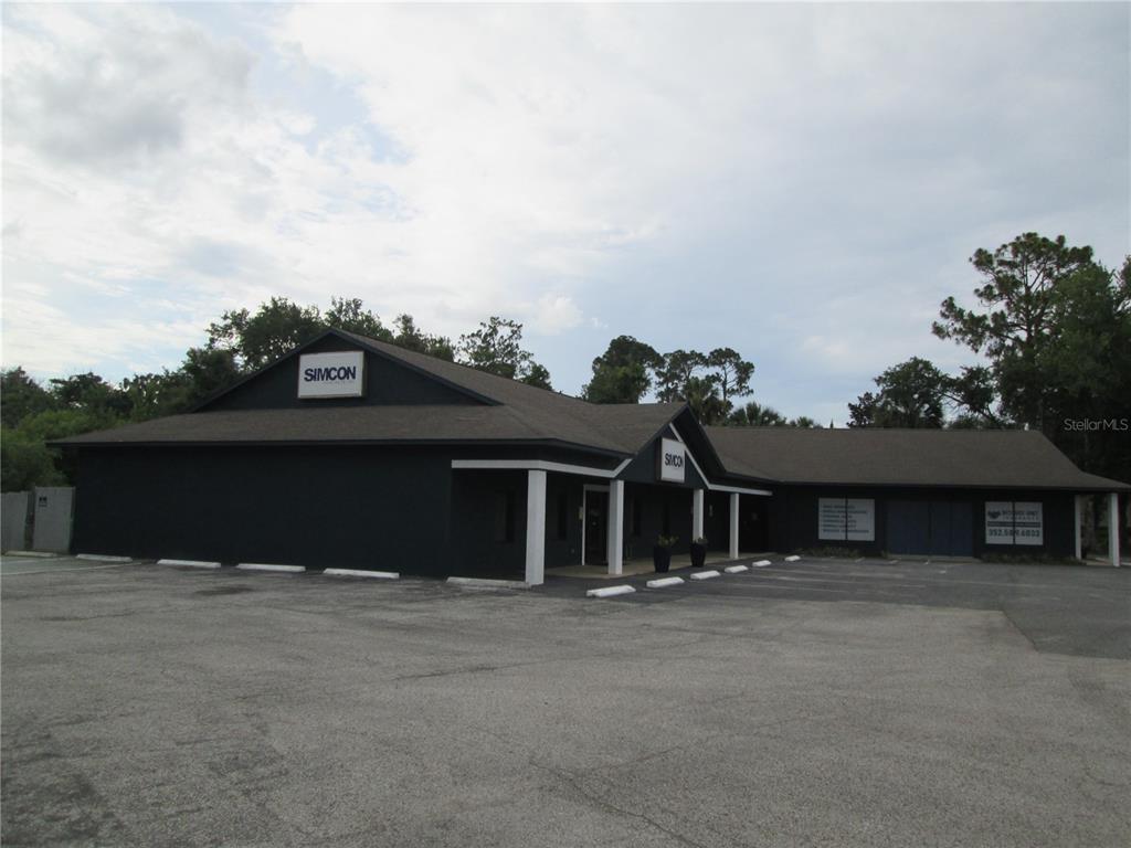 A dark-painted commercial building with a gabled roof and a paved parking lot — 100 W BURLEIGH BOULEVARD, TAVARES, FL