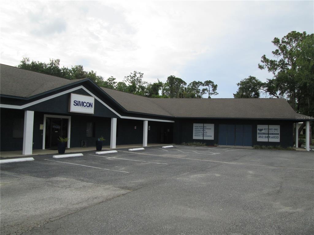 A dark-colored commercial building with a parking lot in front and signage for two businesses — 100 W BURLEIGH BOULEVARD, TAVARES, FL