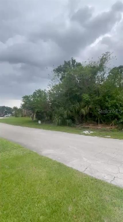 A vacant, tree-covered lot sits along a paved residential street under a cloudy sky — 4153 SW WEBB STREET, PORT ST LUCIE, FL