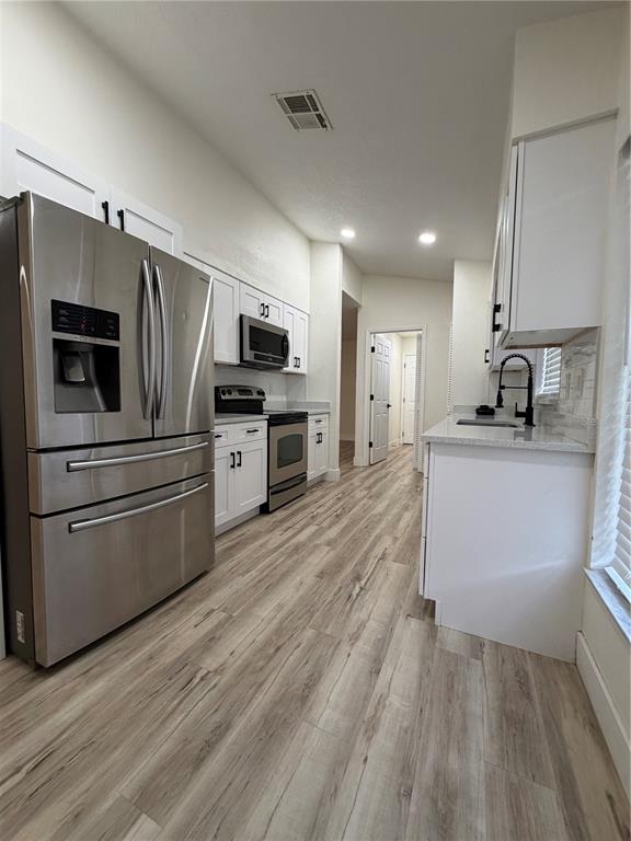 A galley kitchen features white cabinets, stainless steel appliances, and light wood-look flooring — 339 PEMBROKE LANE S UNIT 228, VENICE, FL