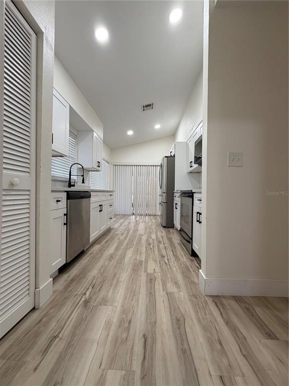 A galley-style kitchen features white cabinets, stainless steel appliances, and light wood-look flooring — 339 PEMBROKE LANE S UNIT 228, VENICE, FL