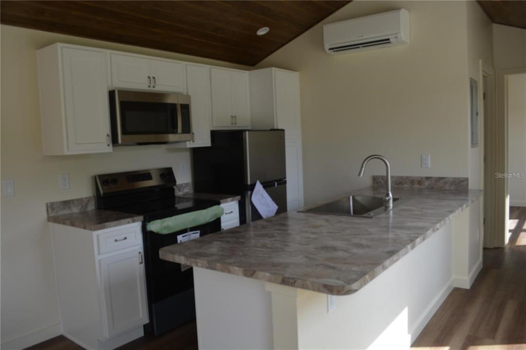 A kitchen features white cabinets, stainless steel appliances, a stone-look countertop, and a wood ceiling — 620 THIRD STREET, OVIEDO, FL