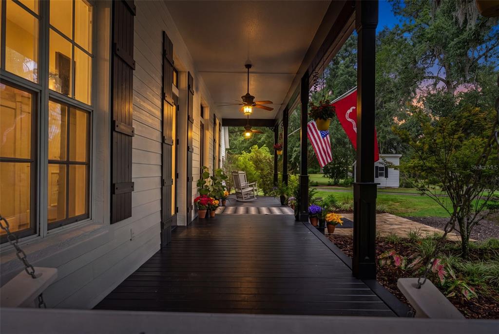 A white house with black trim features a covered porch, rocking chairs, and two flags — 17163 BENES ROUSH ROAD, BROOKSVILLE, FL