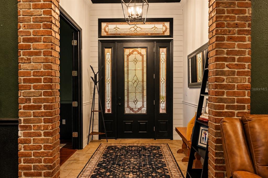 A front porch features a black door, rocking chair, potted plants, and two hanging flags — 17163 BENES ROUSH ROAD, BROOKSVILLE, FL