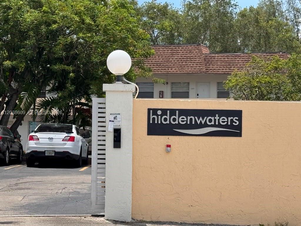 A white gate and a peach-colored wall with a hiddenwaters sign stand outside — 1860 Venice Park Dr # 208, North Miami FL 33181, NORTH MIAMI, FL