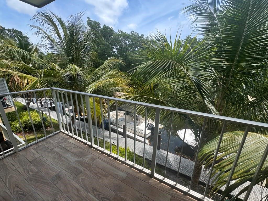 A balcony with wood-look tile flooring overlooks a canal with docked boats and palm trees — 1860 Venice Park Dr # 208, North Miami FL 33181, NORTH MIAMI, FL