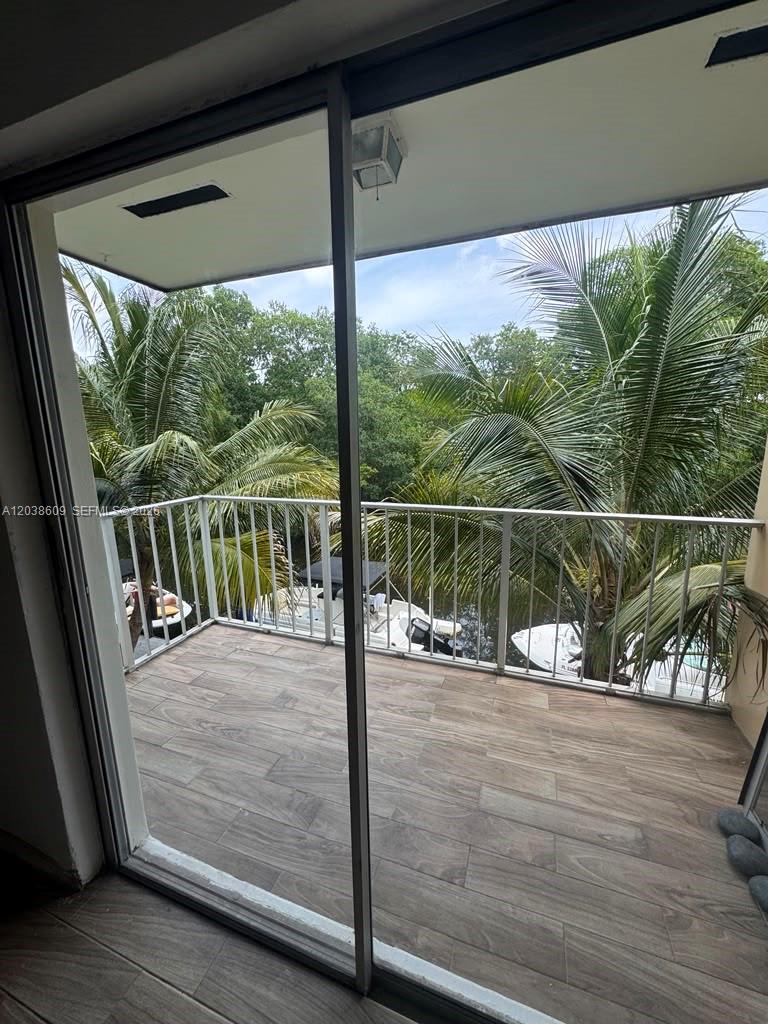 A balcony with wood-look tile flooring overlooks palm trees and boats on a canal — 1860 Venice Park Dr # 208, North Miami FL 33181, NORTH MIAMI, FL