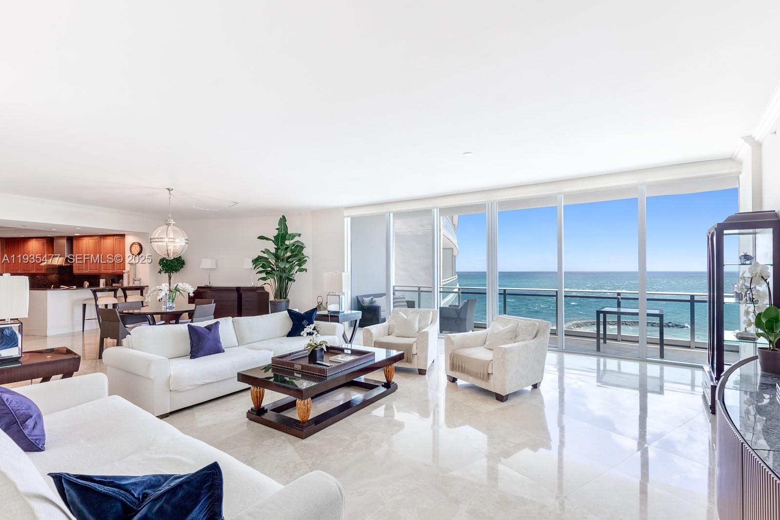 A bright living room features white sofas, marble floors, and floor-to-ceiling windows overlooking the ocean — 10295 Collins Ave # 803, Bal Harbour FL 33154, BAL HARBOUR, FL