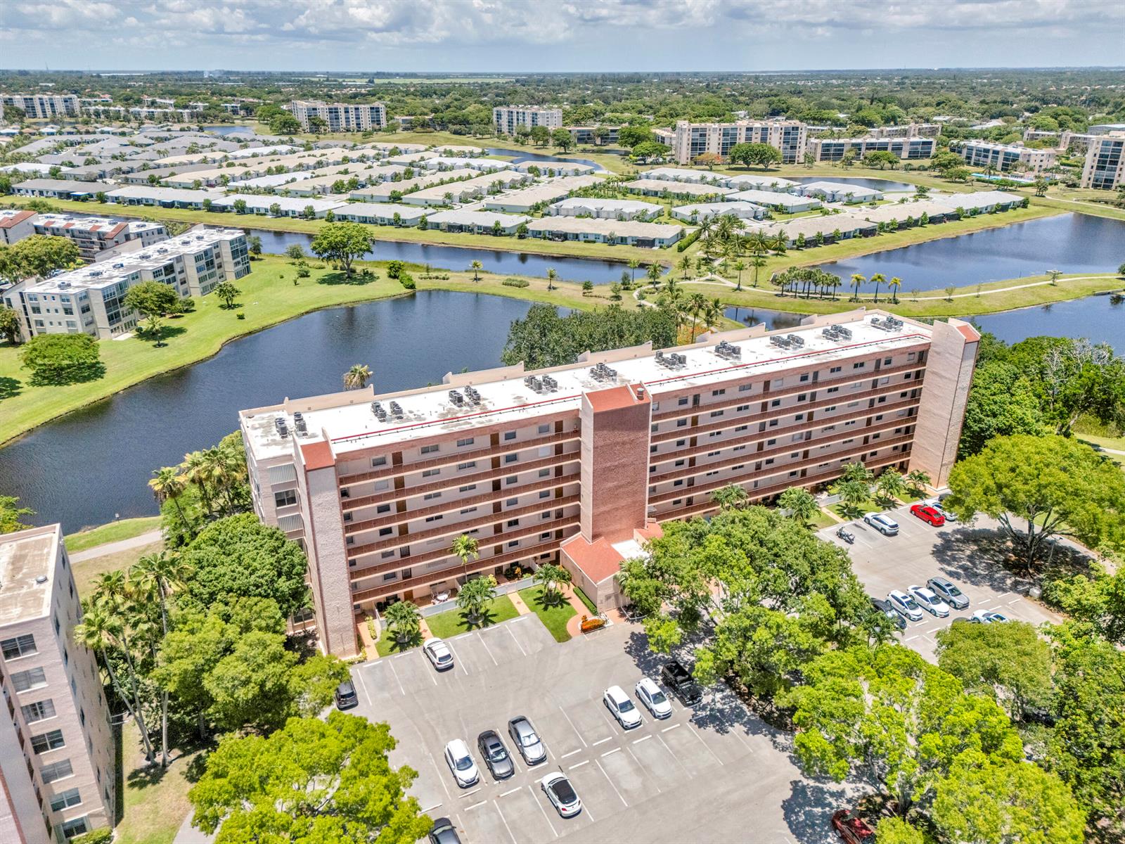 An aerial view shows a multi-story apartment building with a parking lot and surrounding lakes — 14623 Bonaire Boulevard # 203, Delray Beach FL 33446, DELRAY BEACH, FL