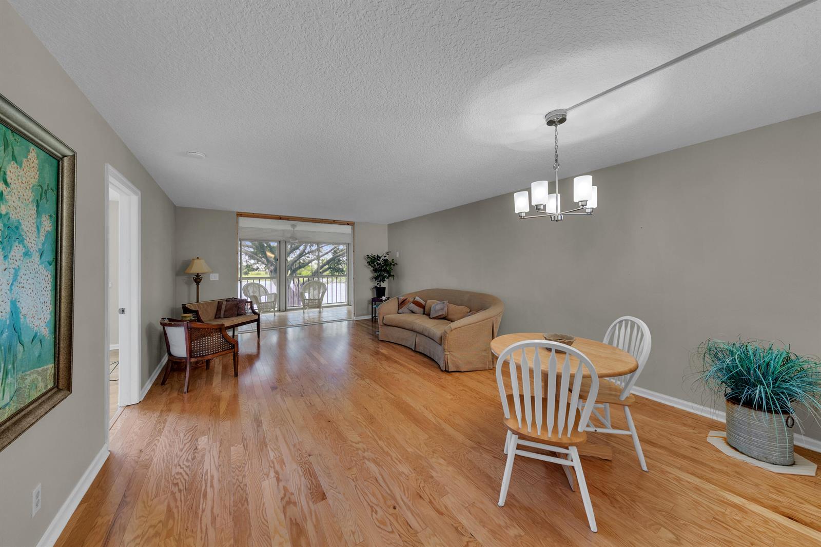 A living and dining area with hardwood floors, a chandelier, and a view of a balcony — 14623 Bonaire Boulevard # 203, Delray Beach FL 33446, DELRAY BEACH, FL