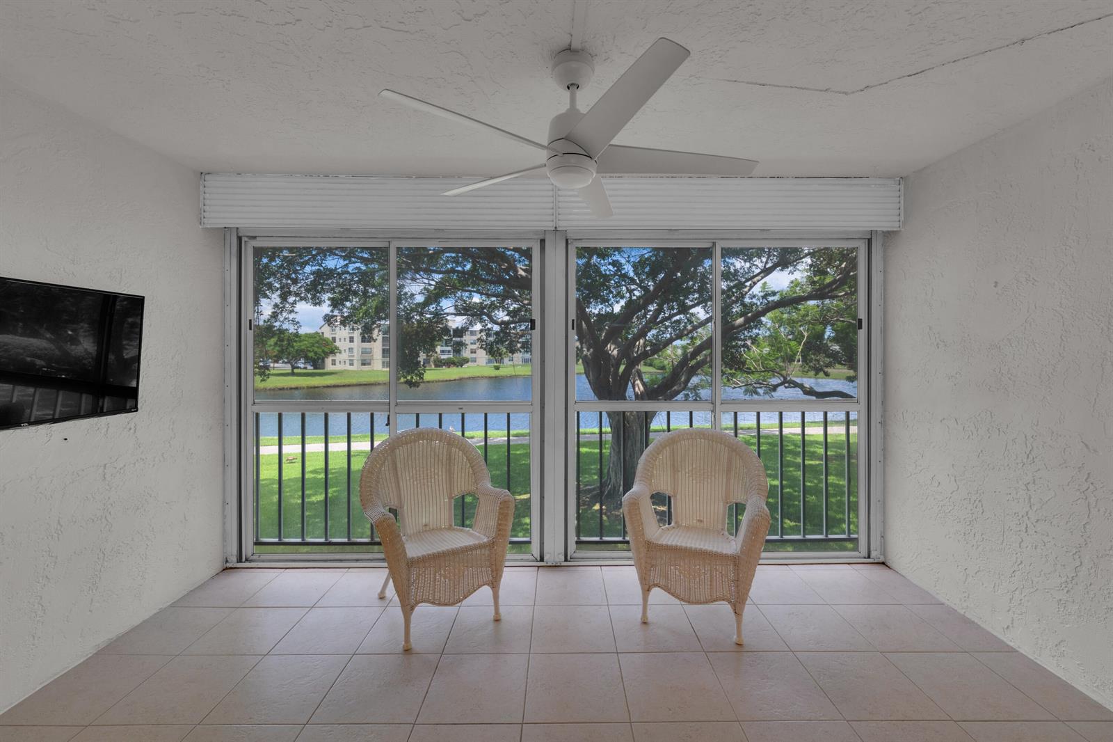 A sunroom with two wicker chairs, a ceiling fan, and sliding glass doors overlooking a lake — 14623 Bonaire Boulevard # 203, Delray Beach FL 33446, DELRAY BEACH, FL