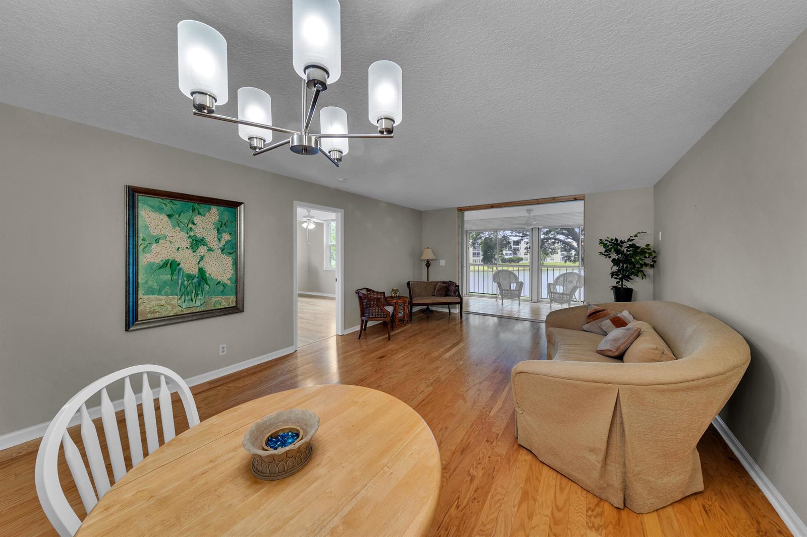 A living and dining area with hardwood floors, a chandelier, and a view of a balcony — 14623 Bonaire Boulevard # 203, Delray Beach FL 33446, DELRAY BEACH, FL