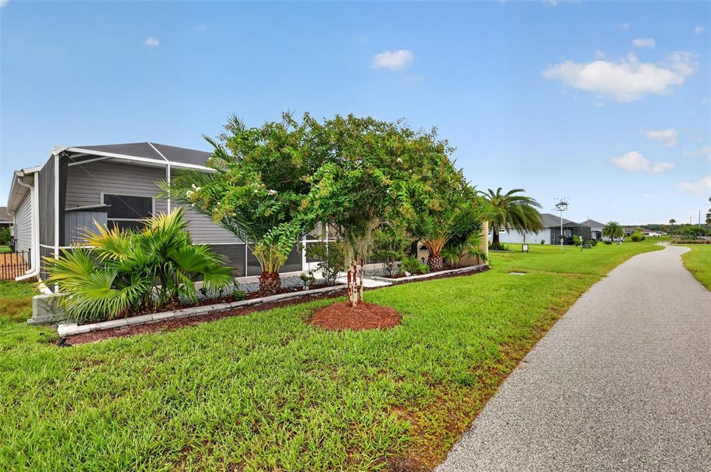 A house with a screened-in patio and landscaping sits next to a paved path — 6033 TOMPKINS STREET, THE VILLAGES, FL