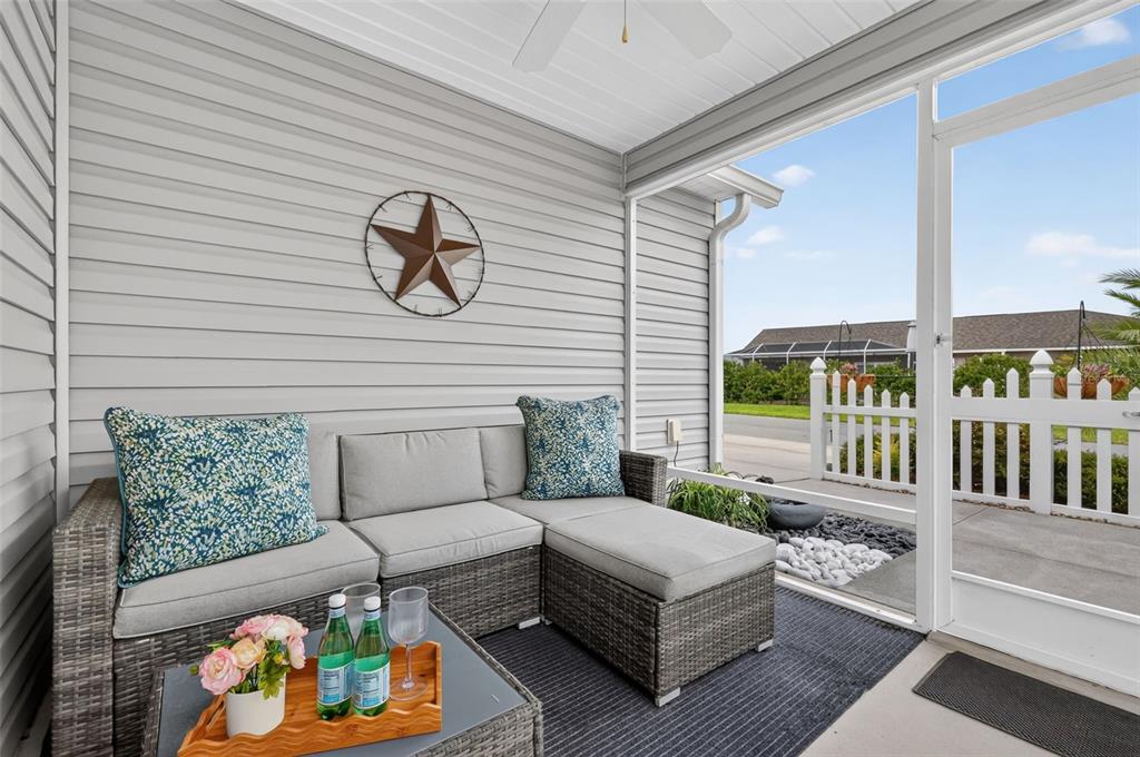 A screened-in porch features gray wicker sectional seating, a coffee table, and a metal star — 6033 TOMPKINS STREET, THE VILLAGES, FL