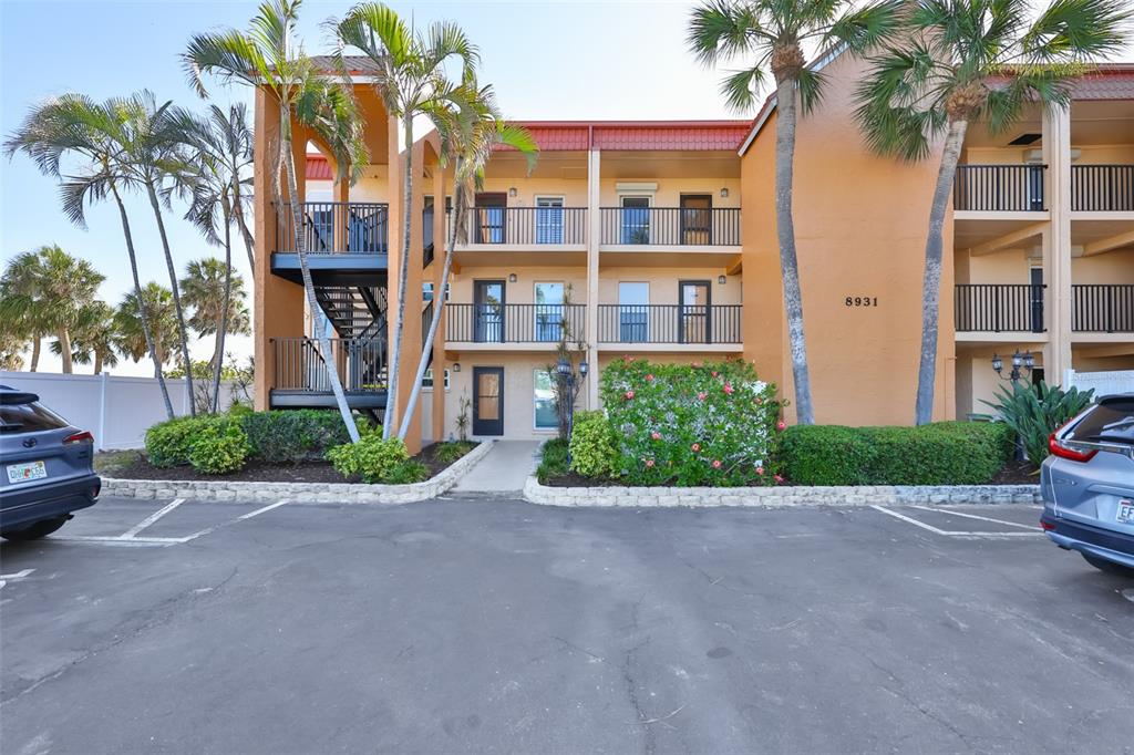 A three-story apartment building with a parking lot and palm trees in the foreground — 8931 BLIND PASS ROAD UNIT 158, ST PETE BEACH, FL
